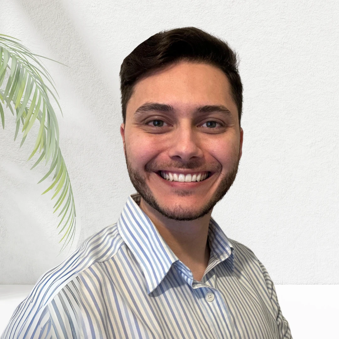 Portrait of Tory Belloise smiling in a striped shirt, with a palm frond beside him.